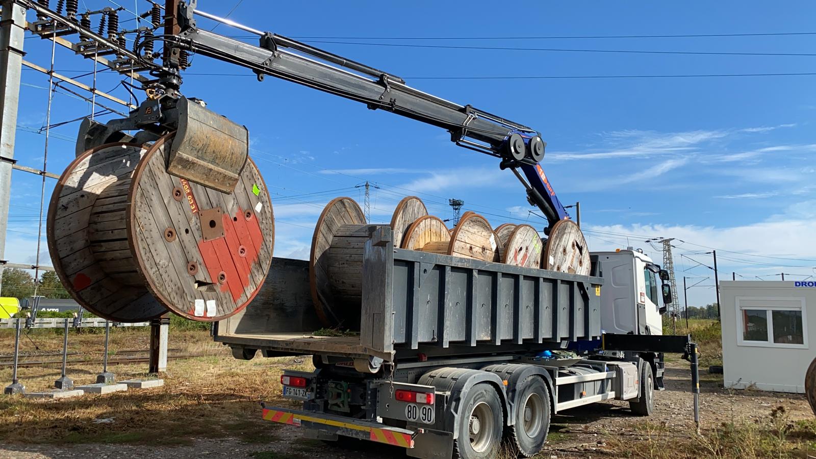 Camion grue chargeant des bobines de cable sur site ferroviaire